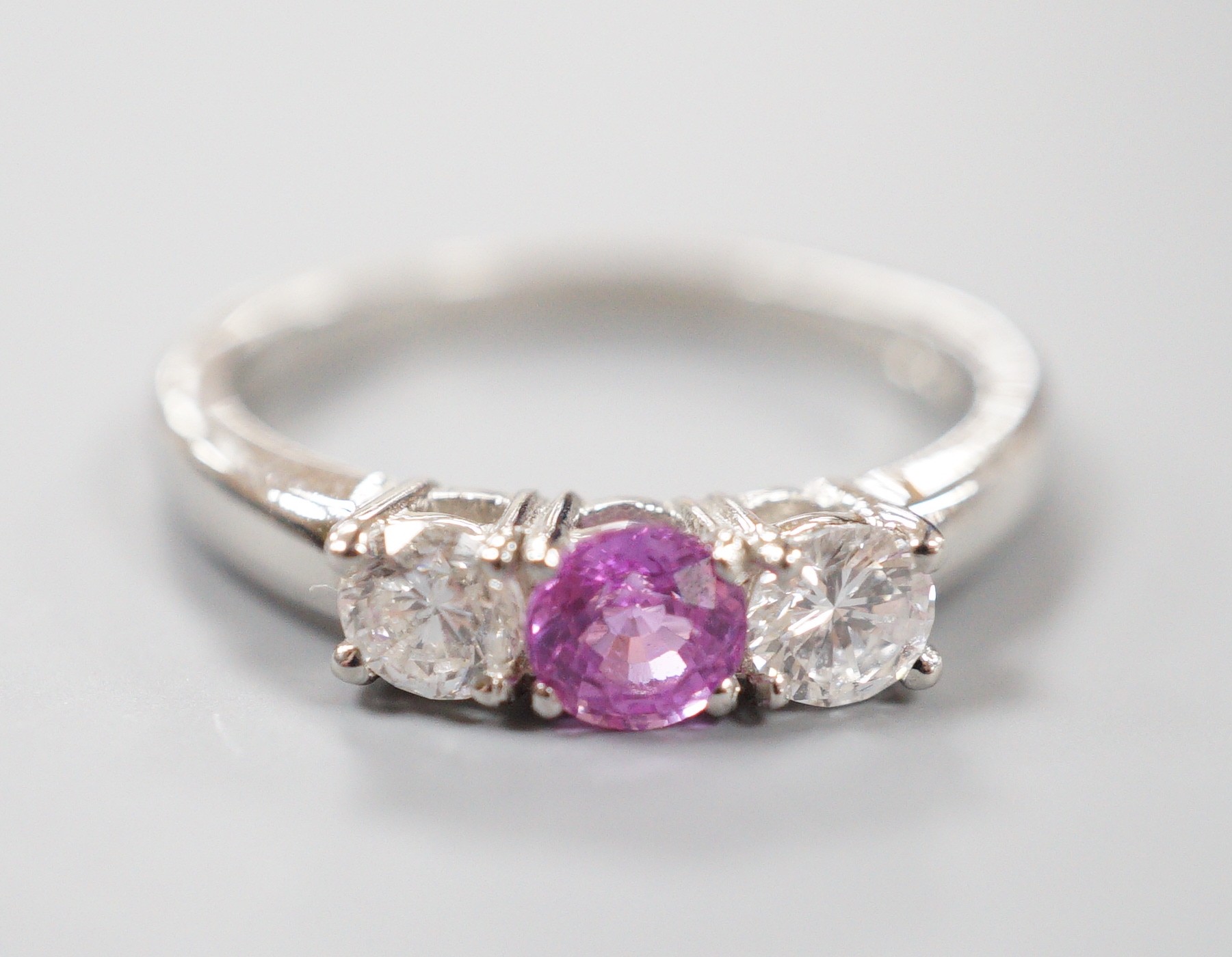 A modern platinum, pink sapphire and two stone round cut diamond set ring, size O, gross weight 5.4 grams